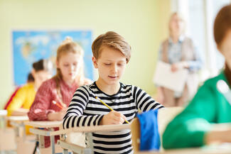 a young boy sits and works at a desk in a classroom