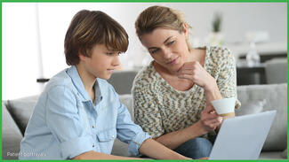 Boy typing on a laptop while his mom looks at screen
