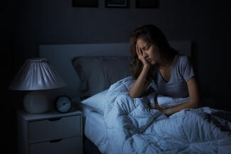 a woman sits up in bed holding her head insomnia