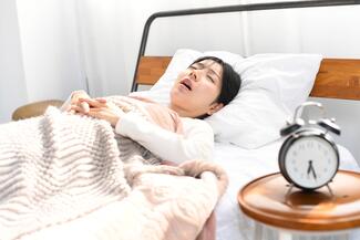A woman lies in bed with her mouth open snoring sleep apnea