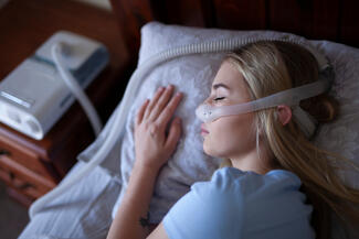 a woman with OSA sleeps in bed wearing CPAP machine