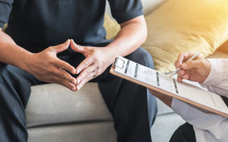 A patient sits across from a doctor who has a clipboard and is filling out a phone