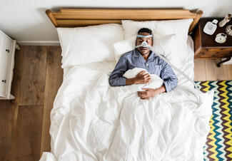 a man lies in bed sleeping while wearing a CPAP machine