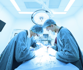 Two surgeons in an operating room under lighting focused on a case.