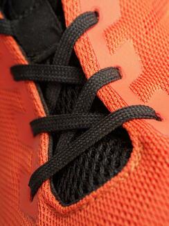 Running shoe in orange and black colors focusing on the laces