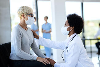 An elderly woman sits with a doctor, both wear masks alzheimer disease agitation