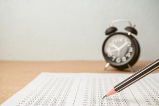 a printed test, pencil, and clock on a desk