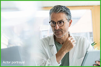 A male doctor in a white coat looking thoughtful