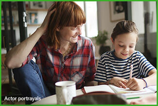 A mother and daughter smile side-by-side while the daughter does homework