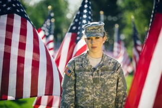 a female soldier stands in front of a row of American flags