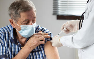 an older man wearing a mask receives a vaccination shot in his upper arm