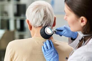 Female doctor views back of older man's neck with a dermatoscope