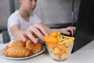 A boy eating junk food while using a laptop computer