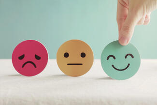 Three illustrated faces, one sad, one neutral, one happy, with a human hand picking up the happy face