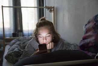 a woman scrolls on her phone while laying in bed