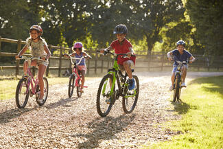 Kids ride their bikes down a dirt path in a grassy field