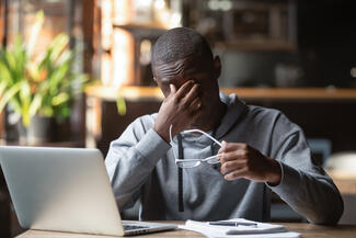 A black man sits in front of a computer looking frustrated with cognitive impairment trouble thinking major depressive disorder