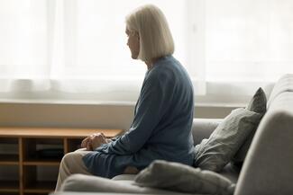 an older woman sits on a couch looking out the window 