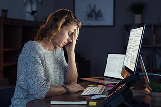a woman holds her hands as she looks at her computer screen