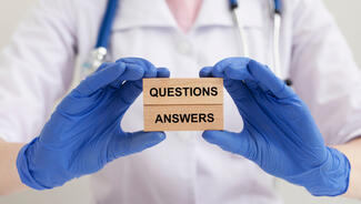 Doctor's gloved hands holding blocks that say "Questions" and "Answers"