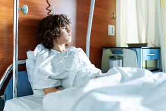 teen boy with brown, curly hair stares out his window in the hospital